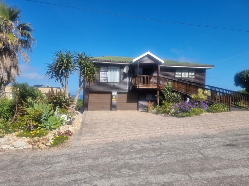 Front elevation of a two-story house featuring corrugated metal cladding, a raised timber deck with staircase, and a paved driveway leading to a double garage.