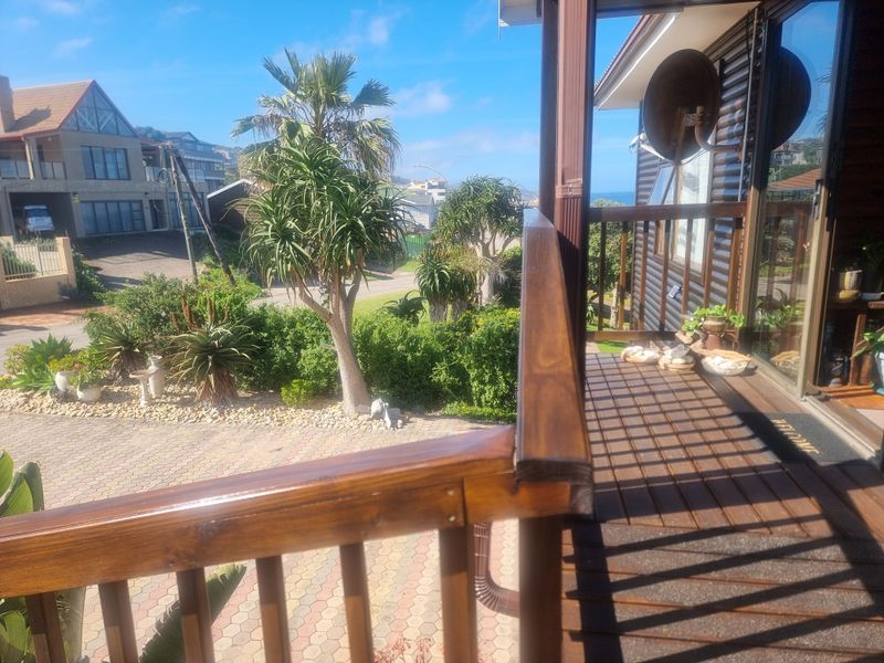 A raised wooden balcony deck with a timber balustrade, overlooking a landscaped garden and driveway area.