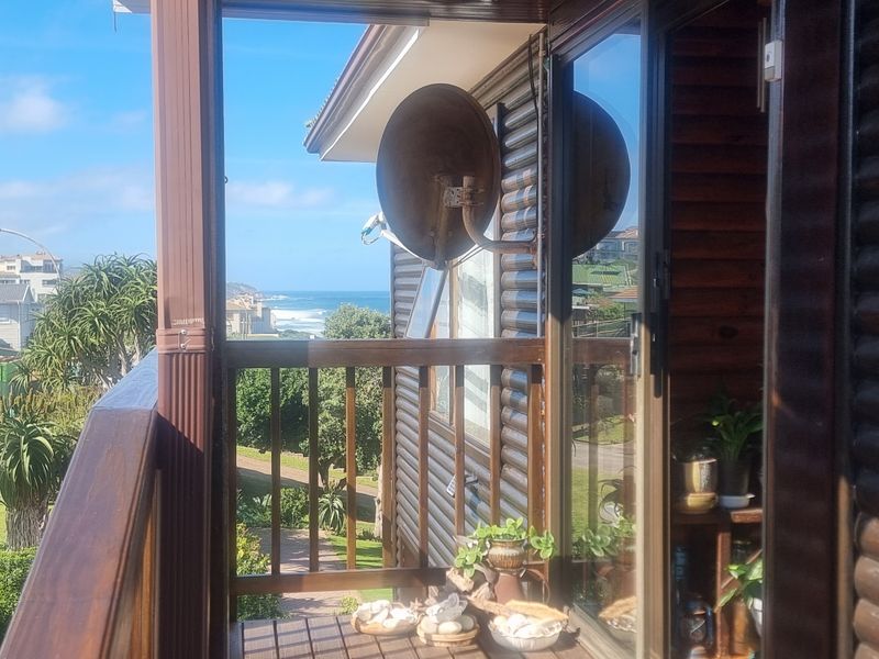 A wooden balcony featuring a balustrade and sliding door access, offering an elevated view of the surrounding coastal landscape.
