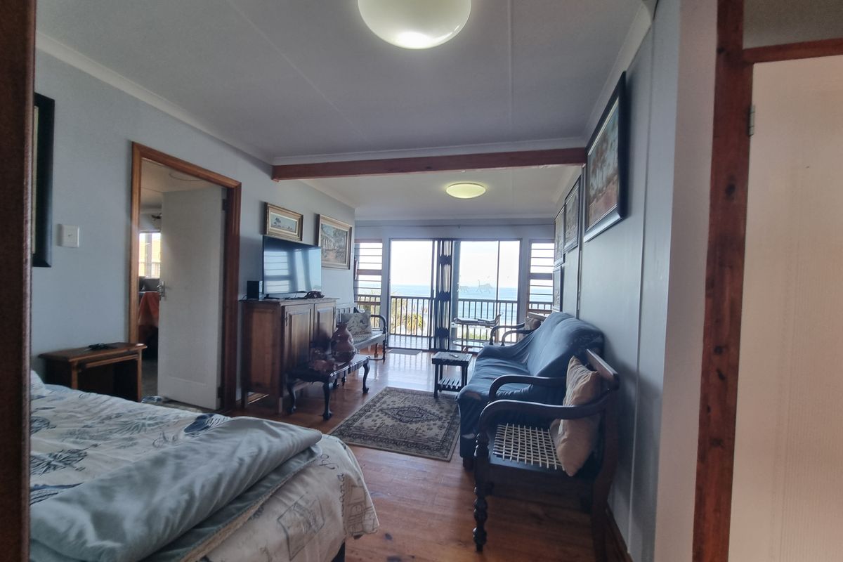 A living area featuring timber flooring, exposed ceiling beams, and sliding glass doors that open to a balcony with ocean views.