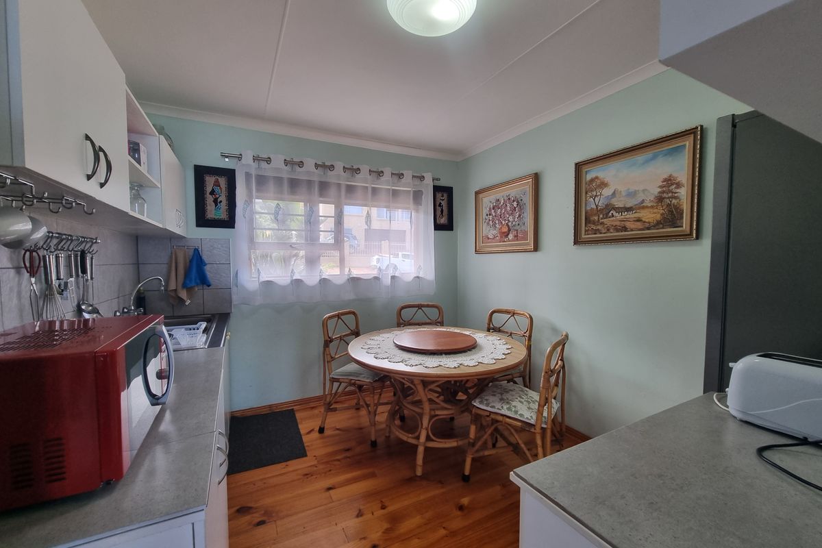 A functional kitchen featuring built-in cabinetry, laminate countertops, a stainless steel sink, and timber flooring, with an integrated dining area.