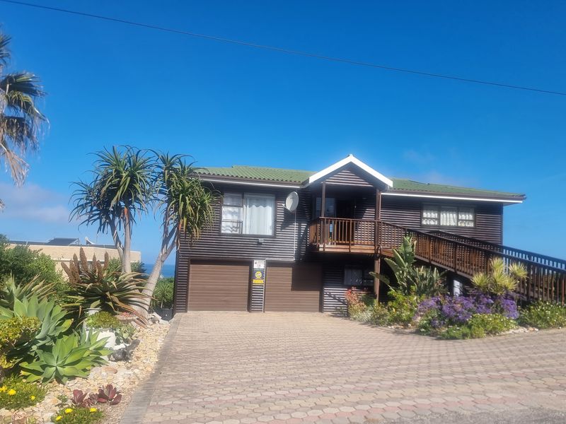 Front elevation of a raised house featuring corrugated metal cladding, a double garage, and a wooden deck with staircase access.