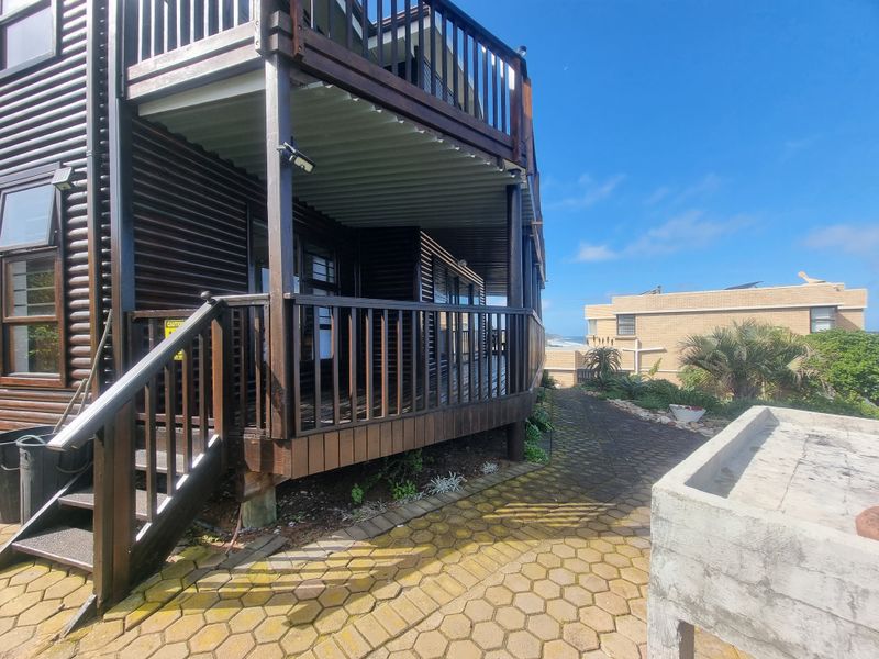 Rear exterior view featuring a multi-level timber deck, paved walkway, and a concrete outdoor basin, showcasing the property's outdoor living space.