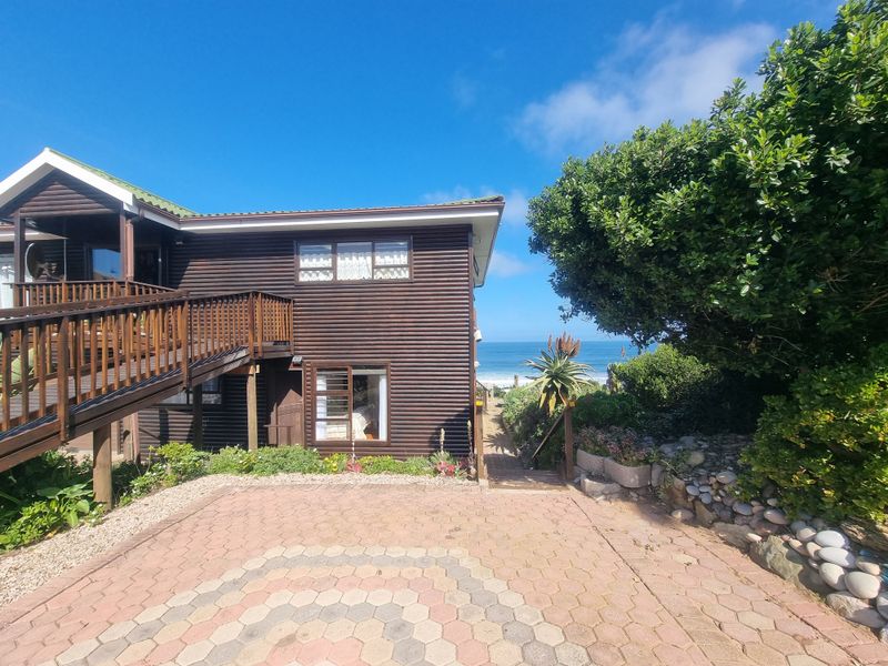 Rear view of a timber-clad house featuring a raised wooden deck, paved driveway, and landscaped garden with ocean views.