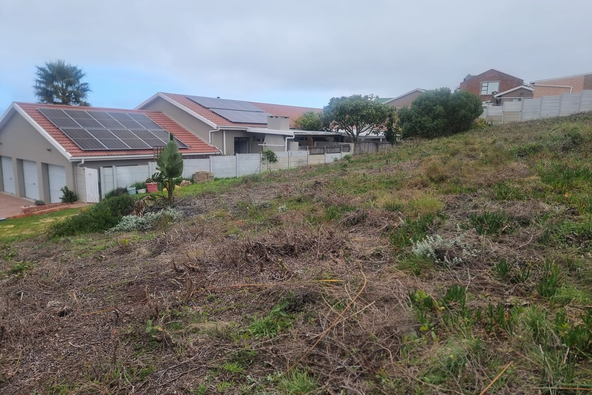 A view of a sloped residential plot adjacent to an existing home featuring solar panels and a secure boundary wall.