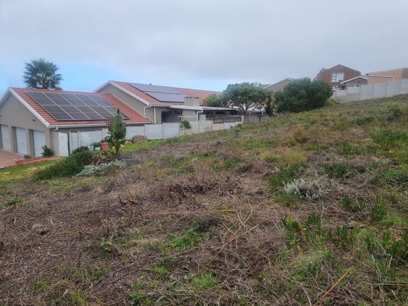 A view of a sloped residential plot adjacent to an existing home featuring solar panels and a secure boundary wall.