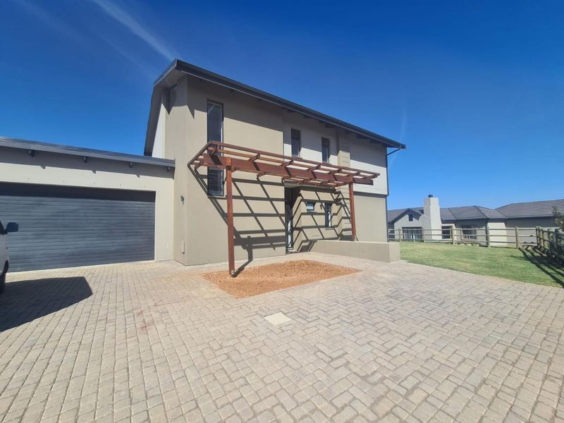 Front exterior view of a modern house featuring a paved driveway, double garage, and a wooden pergola structure over the entrance area.