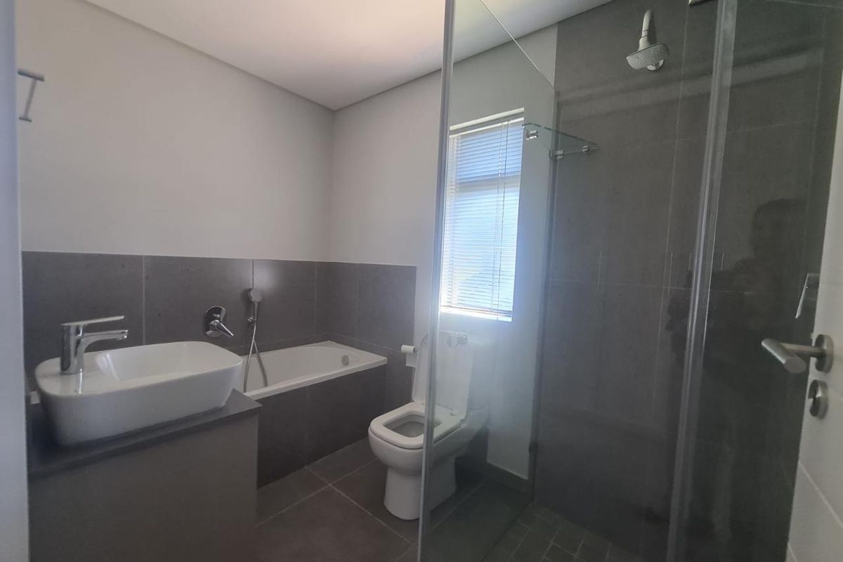 Modern bathroom featuring a vessel sink, built-in bathtub, toilet, and a separate glass-enclosed shower with contemporary grey tiling.