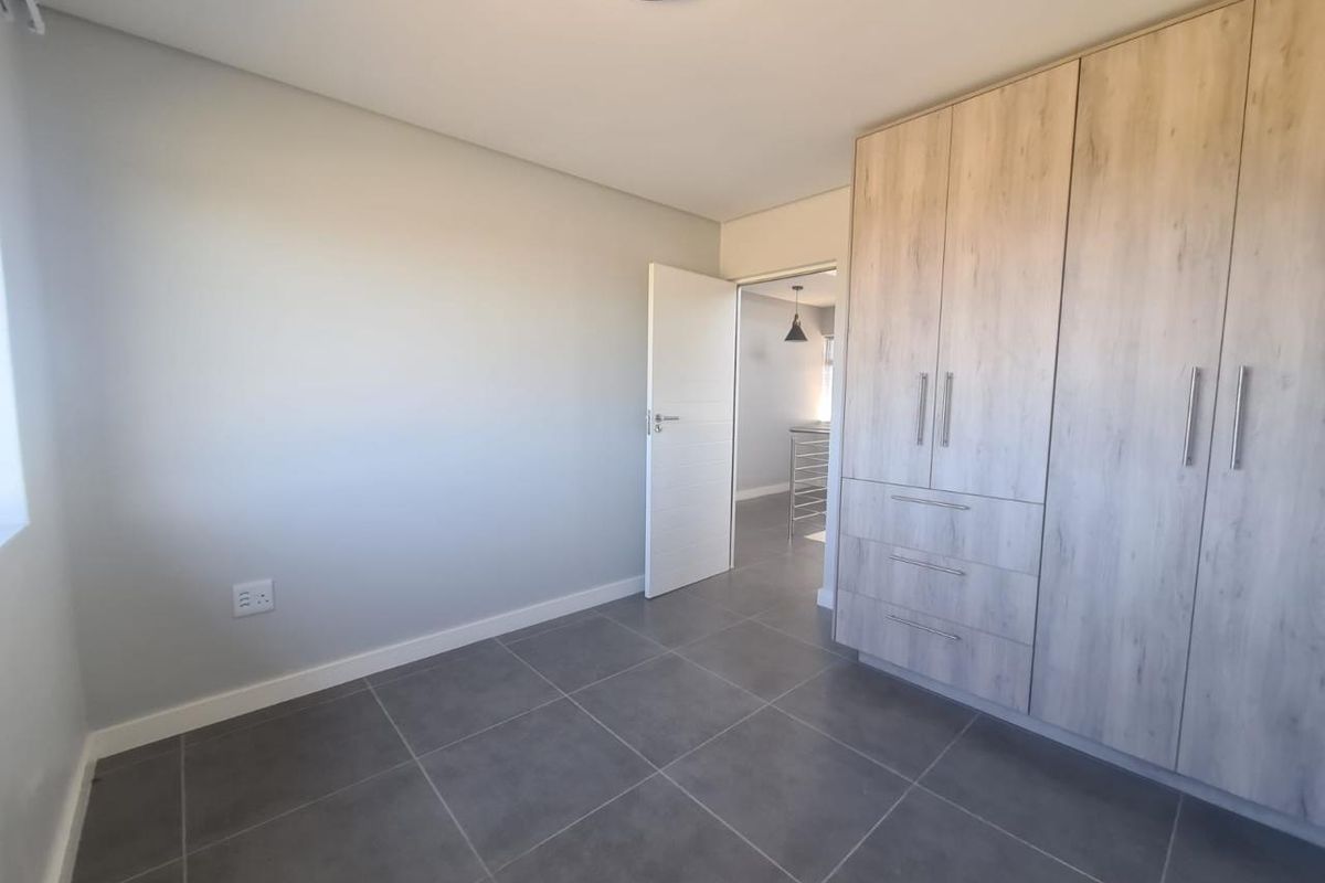 A clean, modern bedroom featuring neutral grey floor tiles, light wood-finish built-in cupboards, and a minimalist aesthetic.