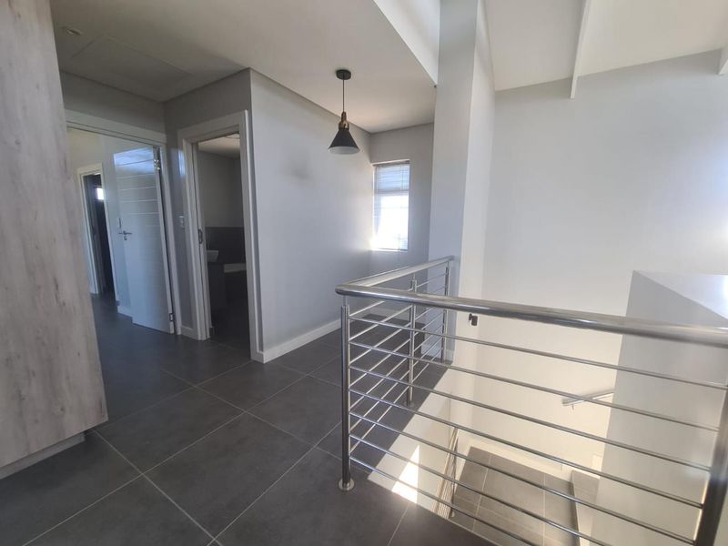 A modern, well-lit upper-level landing featuring sleek stainless steel balustrades, large format floor tiles, and neutral wall finishes.