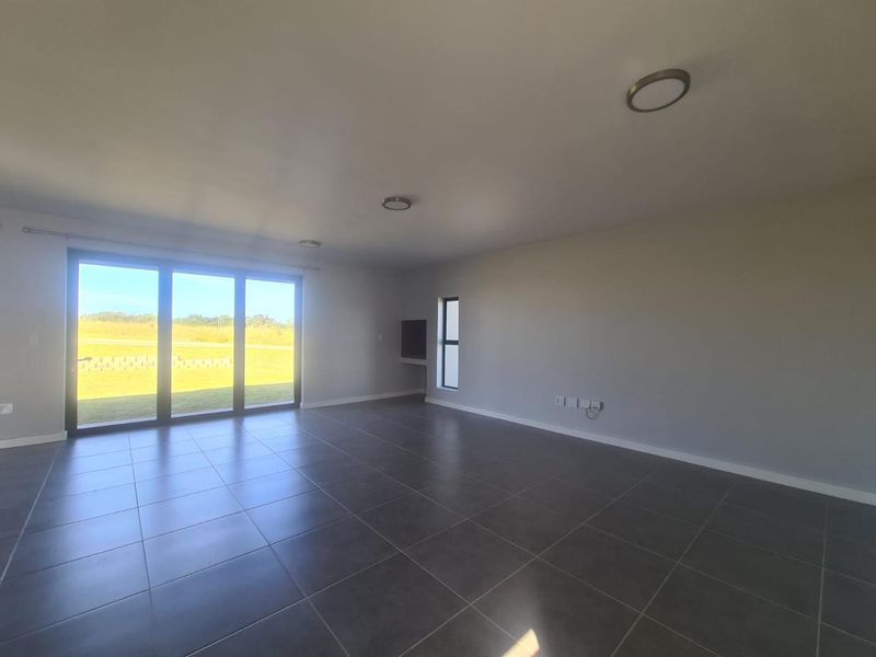 A spacious, empty living area featuring large sliding glass doors, tiled flooring, and modern recessed lighting, offering a bright and open atmosphere.