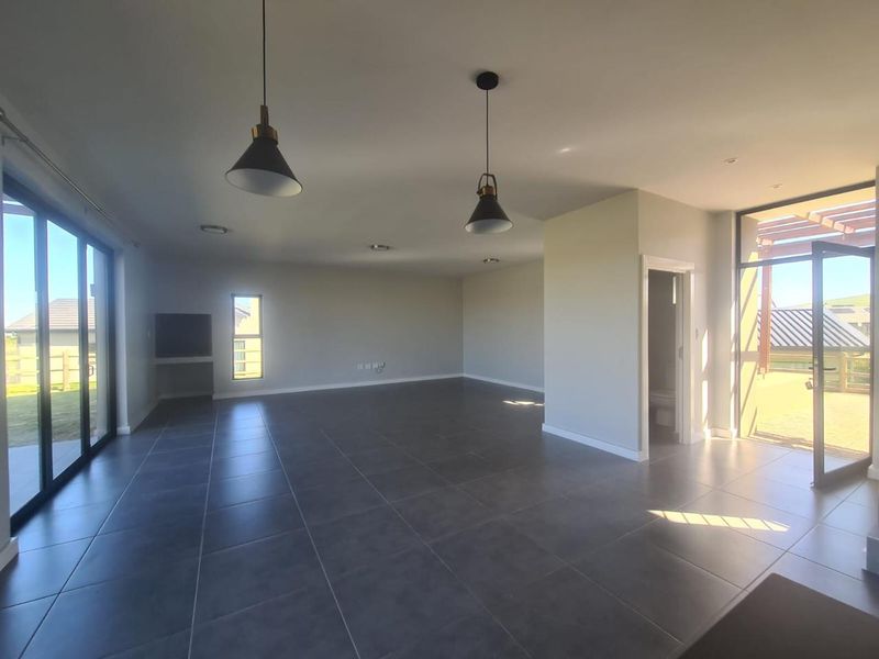 Spacious, modern open-plan living area featuring large format floor tiles, abundant natural light, and direct access to outdoor patio spaces.