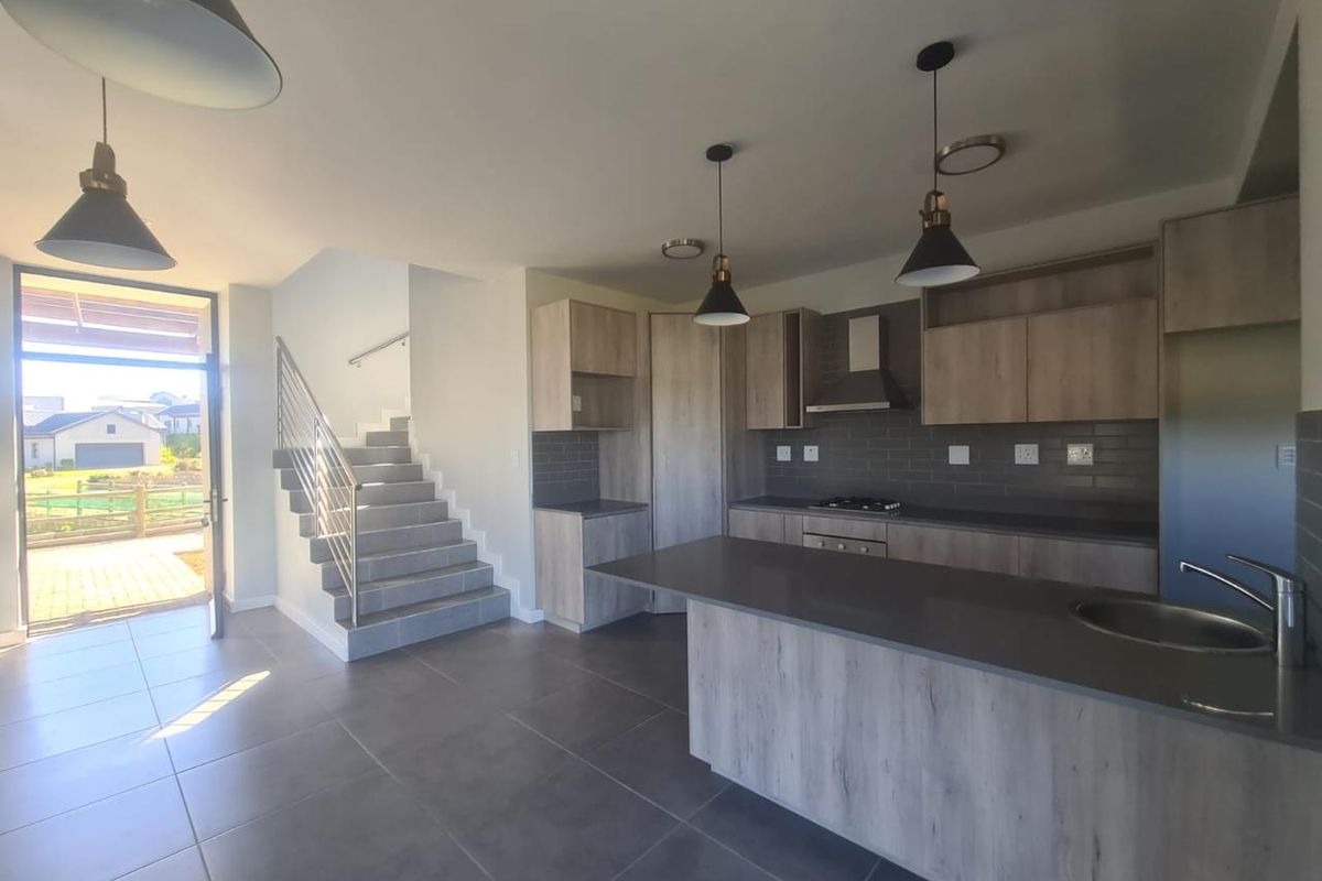 Modern open-plan kitchen featuring light wood cabinetry, stone countertops, and integrated appliances, seamlessly flowing into the living area with direct access to the patio.