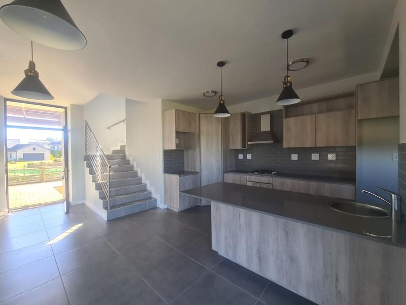 Modern open-plan kitchen featuring light wood cabinetry, stone countertops, and integrated appliances, seamlessly flowing into the living area with direct access to the patio.