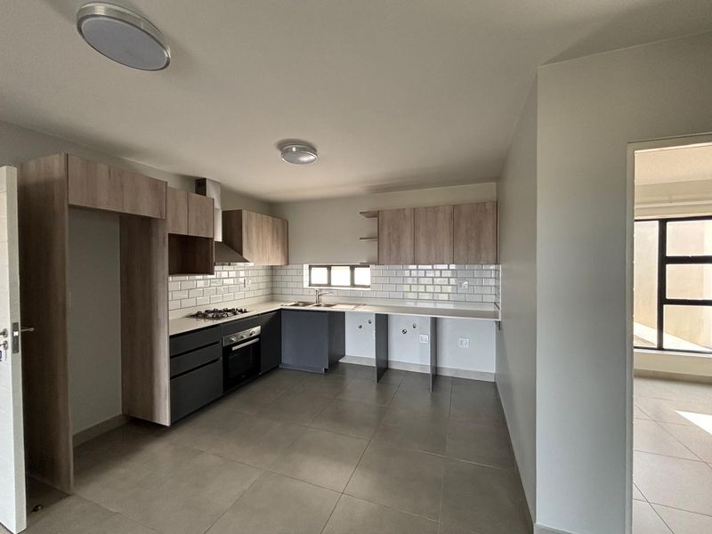 Modern kitchen featuring two-tone cabinetry, subway tile backsplash, gas hob, electric oven, and tiled flooring. The space is clean and ready for appliances.