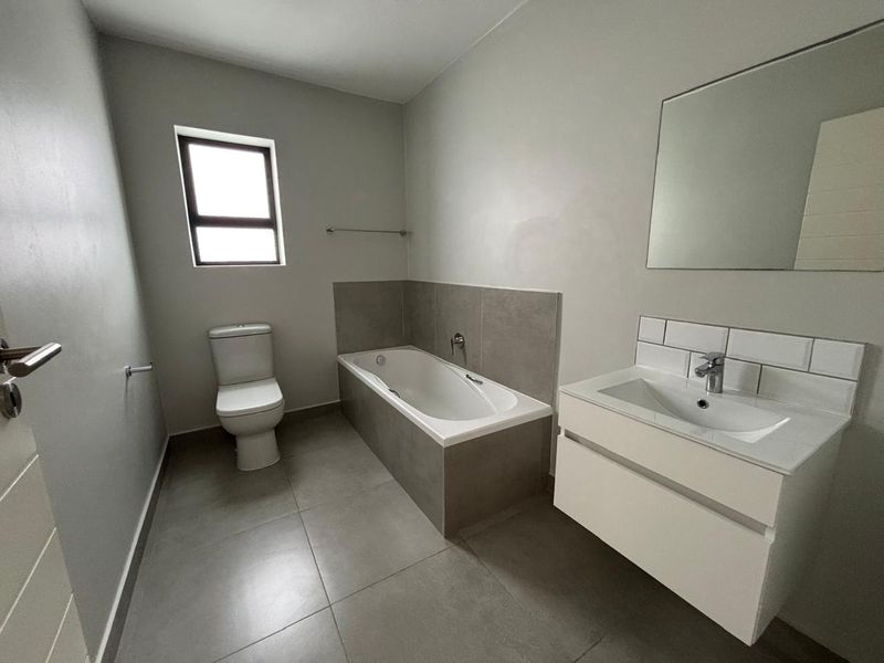 A modern, clean bathroom featuring a built-in bathtub, wall-mounted vanity with basin, and neutral grey floor tiles.