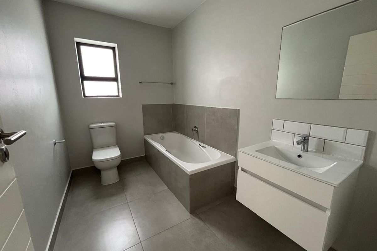 A modern, clean bathroom featuring a built-in bathtub, wall-mounted vanity with basin, and neutral grey floor tiles.