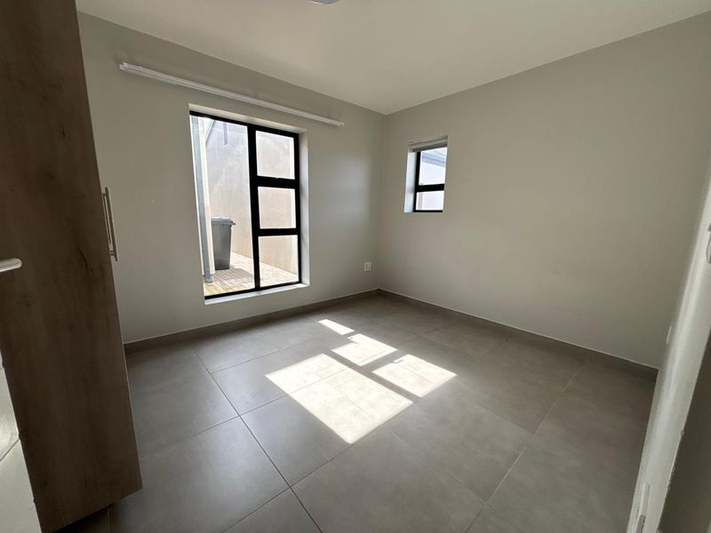 A bright, empty bedroom featuring neutral tiled flooring, built-in cupboard storage, and modern aluminium window frames.
