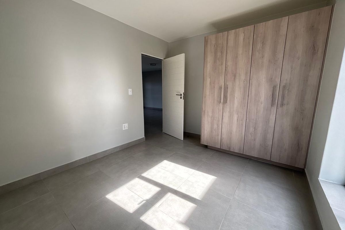 A bright, empty bedroom featuring neutral tiled flooring and modern built-in wooden cupboards, offering a clean and versatile living space.