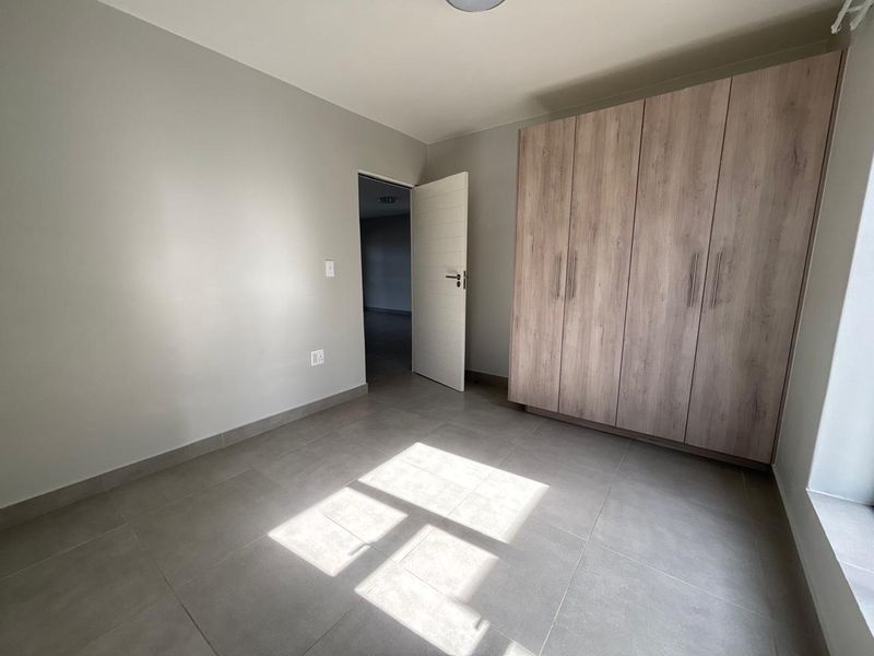 A bright, empty bedroom featuring neutral tiled flooring and modern built-in wooden cupboards, offering a clean and versatile living space.