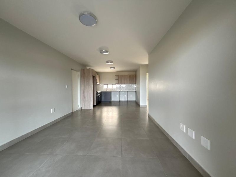 An open-plan living and kitchen area featuring neutral tiled flooring, modern cabinetry, and a subway tile backsplash in a clean, vacant space.