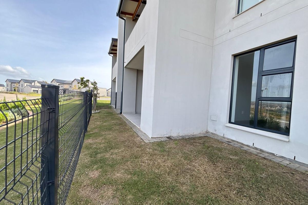 Rear exterior view of the apartment building featuring a covered patio, paved border, and wire mesh perimeter fencing.