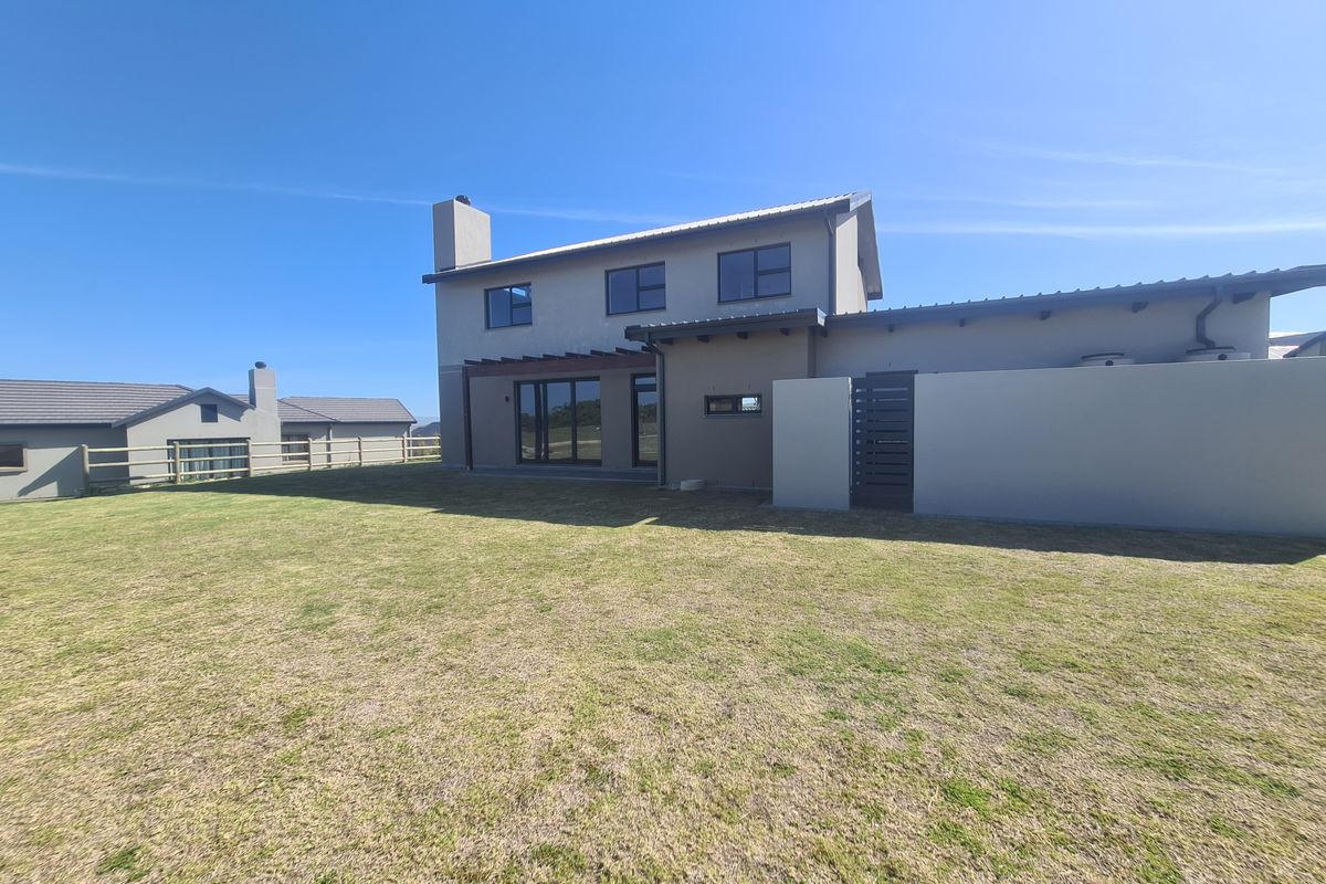 Rear view of a modern two-story house featuring a timber pergola, large sliding glass doors, and a spacious private lawn area.