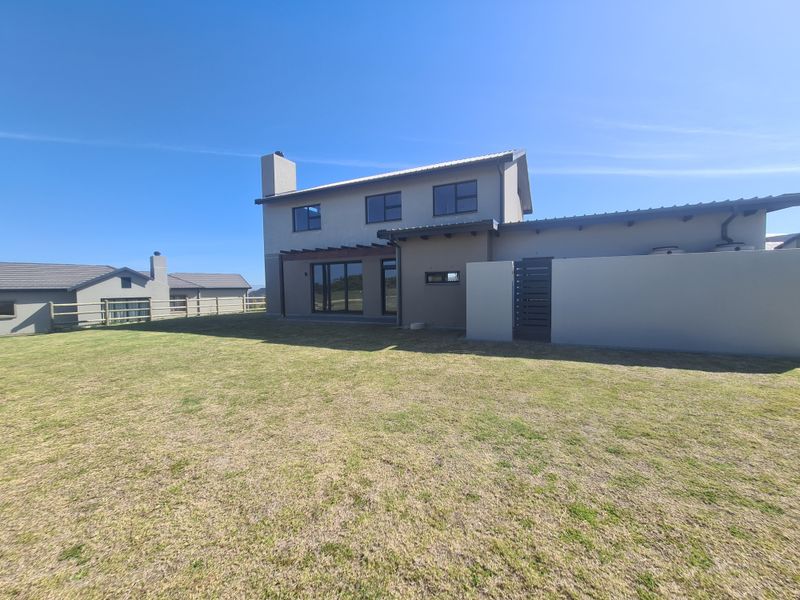Rear view of a modern two-story house featuring a timber pergola, large sliding glass doors, and a spacious private lawn area.