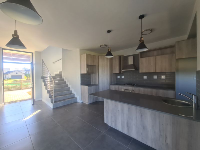 Modern open-plan kitchen featuring wood-look cabinetry, stone countertops, and integrated appliances, seamlessly flowing into the living area with direct access to the patio.