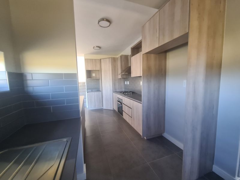 Modern kitchen featuring light wood-tone cabinetry, dark tiled flooring, subway tile backsplash, and integrated appliances including a gas hob and oven.