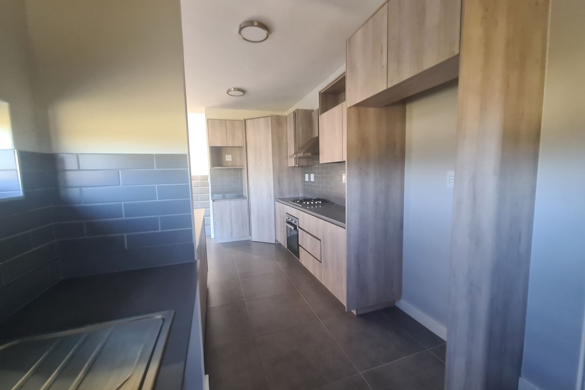 Modern kitchen featuring light wood-tone cabinetry, dark tiled flooring, subway tile backsplash, and integrated appliances including a gas hob and oven.