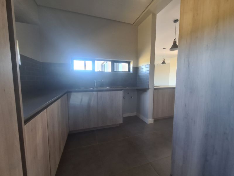 A clean, modern scullery featuring built-in cabinetry, a subway tile backsplash, and a stainless steel sink, with tiled flooring throughout.