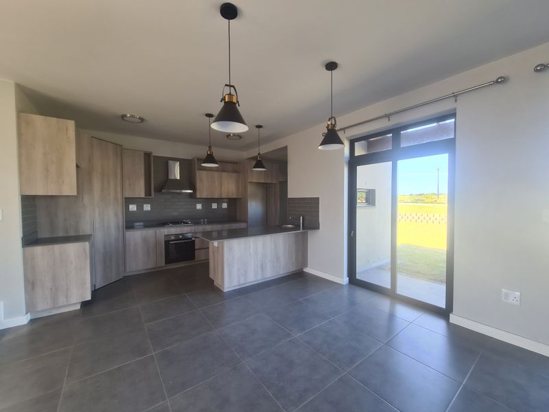 Modern open-plan kitchen featuring wood-look cabinetry, a central island, built-in appliances, and direct access to the outdoor area through a large sliding glass door.