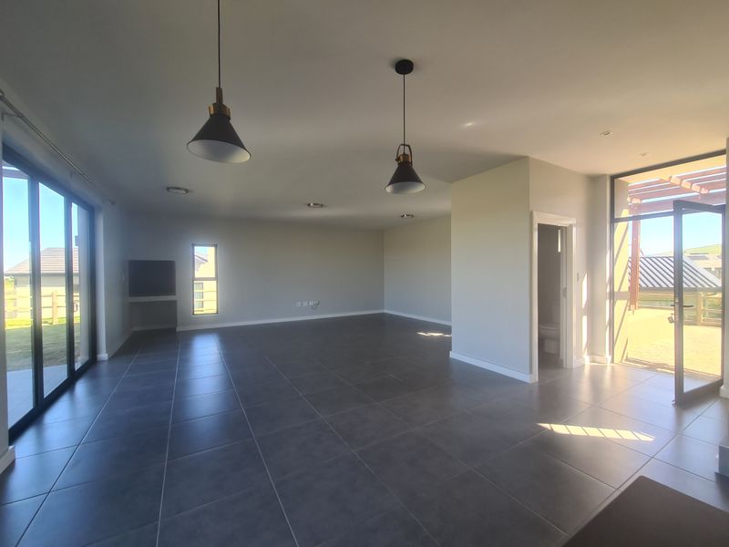 Spacious, open-plan living area featuring large format floor tiles, modern pendant lighting, and dual access to outdoor patio spaces through sliding glass doors.