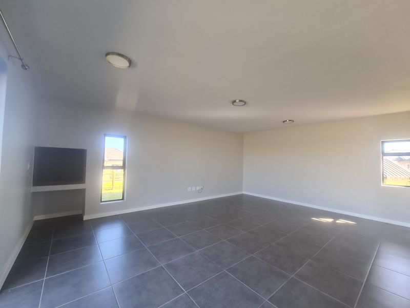 A spacious, empty living area featuring modern dark floor tiles, neutral walls, recessed lighting, and a built-in wall niche.