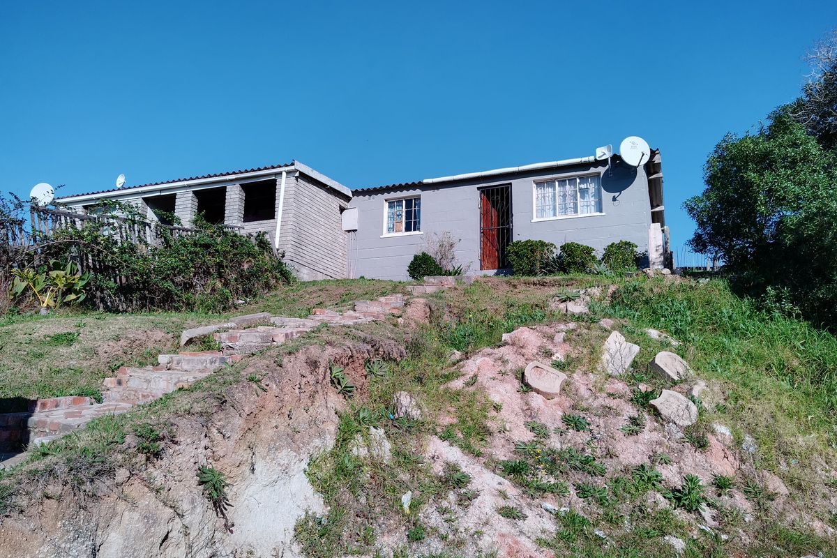 Rear view of a single-story house featuring a brick staircase leading up an eroded embankment to the dwelling entrance.