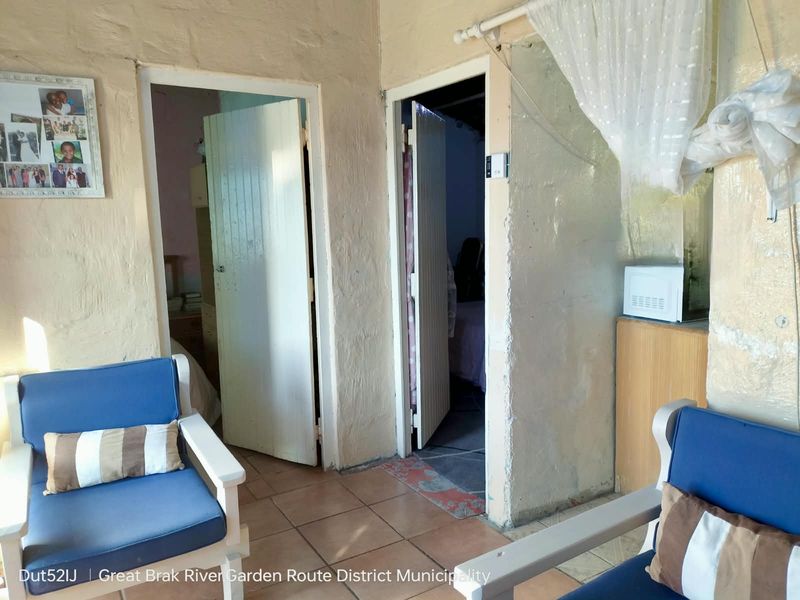 A living area featuring tiled flooring and access to two adjacent rooms, showing signs of dated wall finishes and general wear.