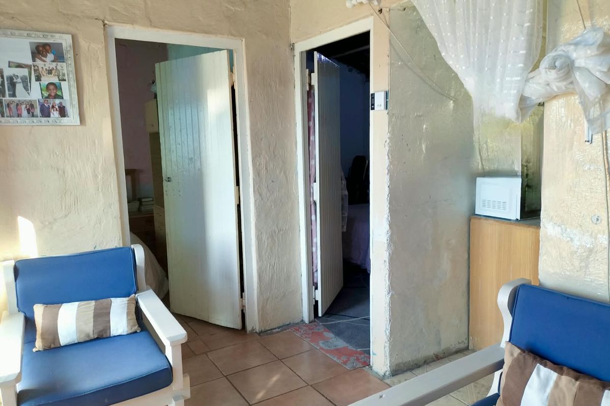 A living area featuring tiled flooring and access to two adjacent rooms, showing signs of dated wall finishes and general wear.