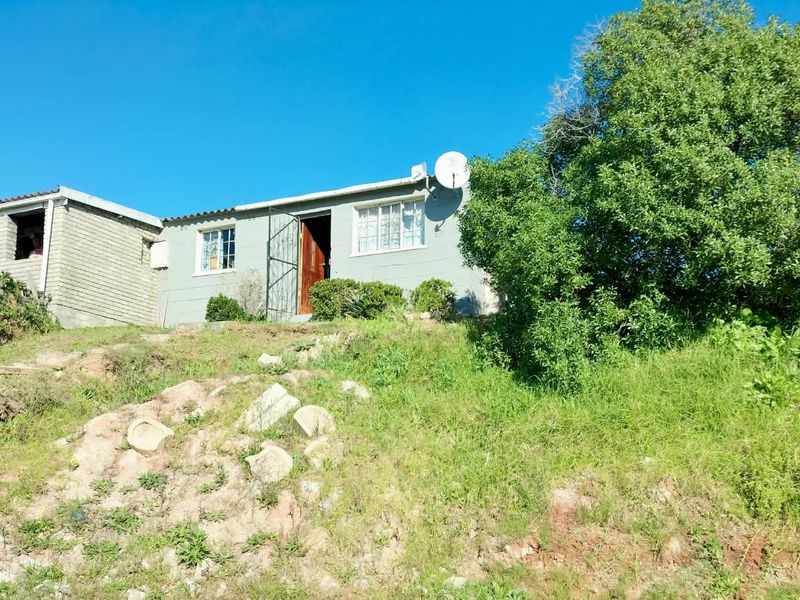 Front exterior view of a single-story house featuring a satellite dish and security gate, situated on an elevated, unlandscaped plot.