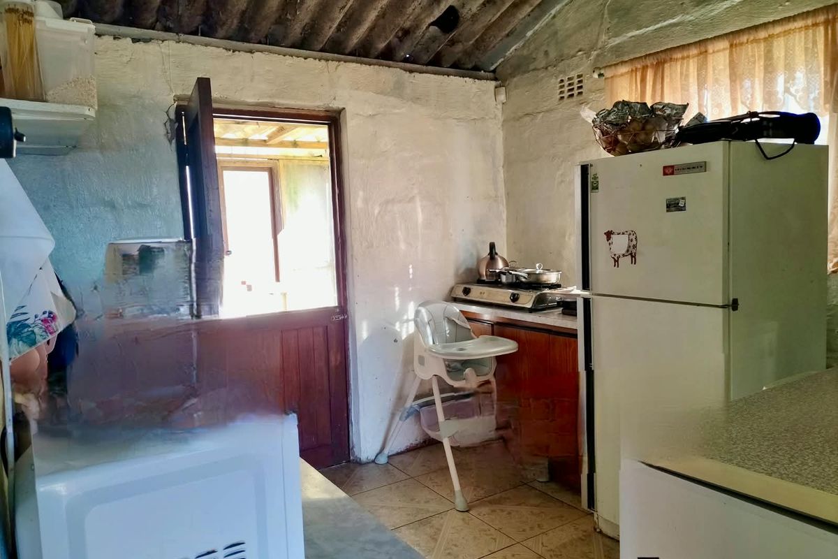 A dated kitchen area featuring tiled floors, built-in cabinetry, and an exposed corrugated roof structure with direct access to an outdoor space.