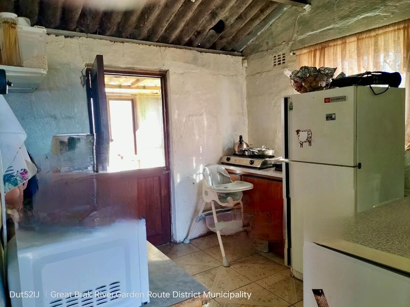 A dated kitchen area featuring tiled floors, built-in cabinetry, and an exposed corrugated roof structure with direct access to an outdoor space.