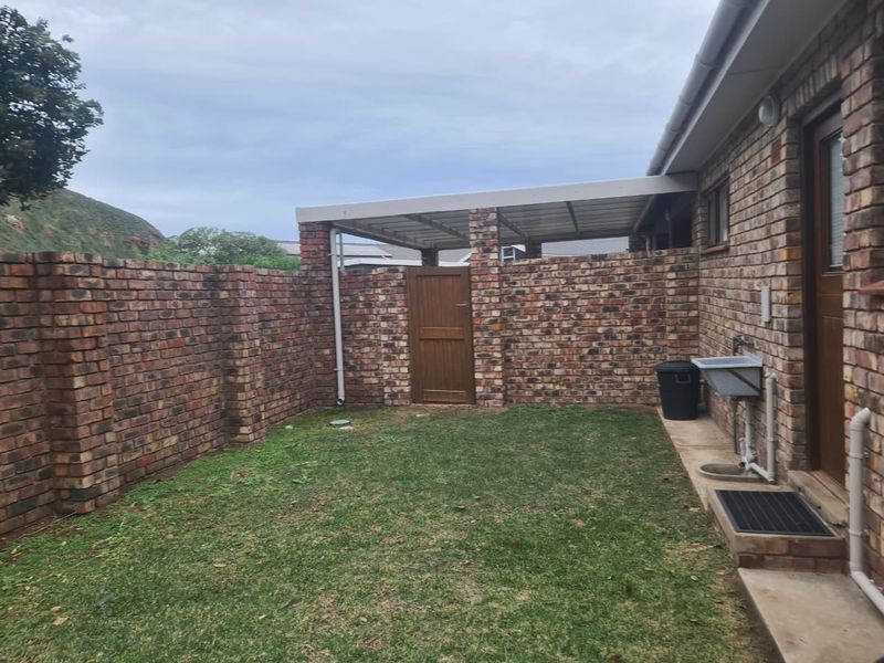 A private rear courtyard featuring a face brick boundary wall, a covered patio area, and an external utility sink.