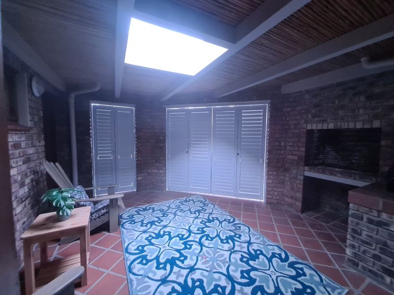 Covered patio area featuring a built-in braai, exposed beam ceiling with a skylight, and shutter doors opening to the exterior.