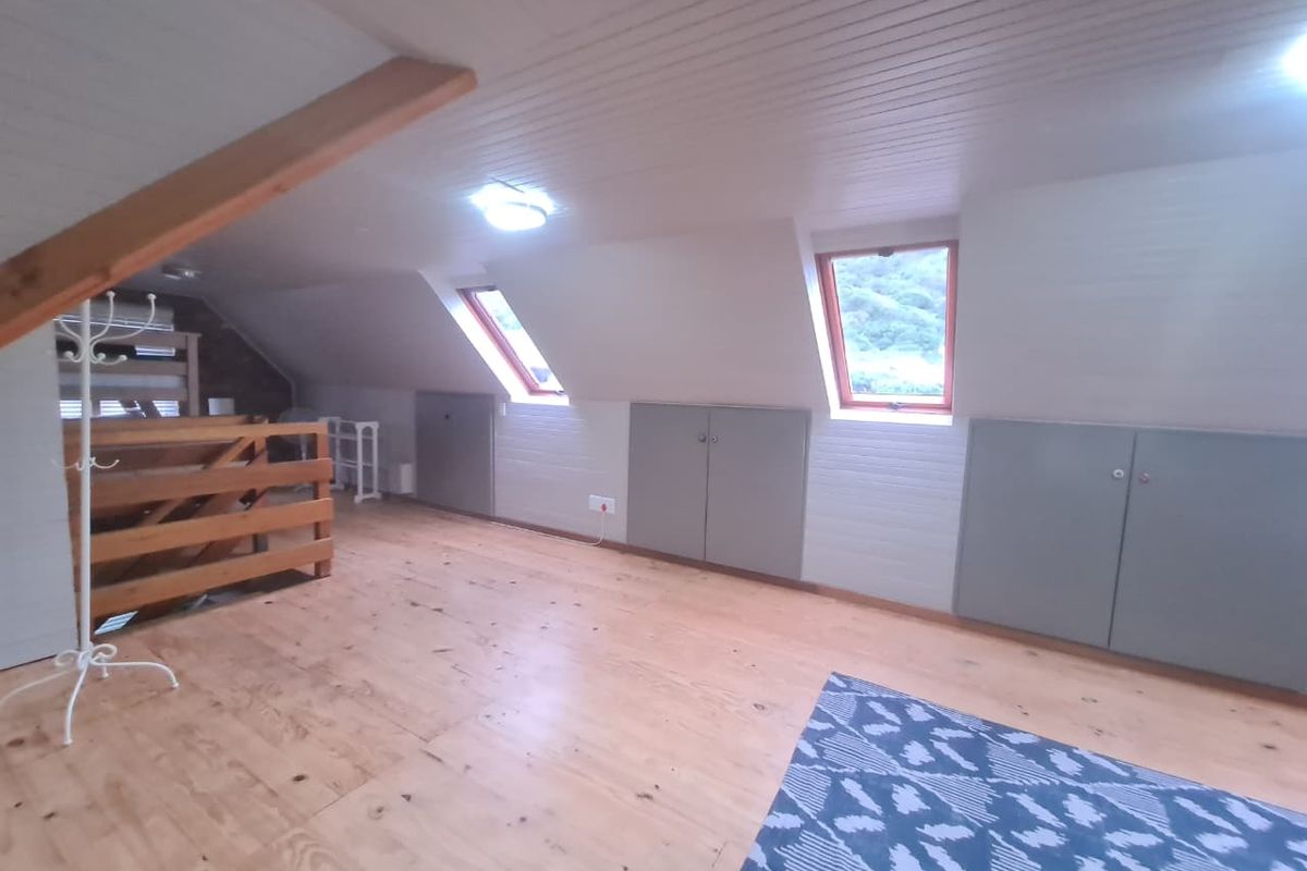 Spacious attic bedroom featuring timber flooring, panelled ceiling, skylight windows, and convenient built-in eaves storage cupboards.
