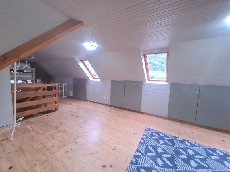 Spacious attic bedroom featuring timber flooring, panelled ceiling, skylight windows, and convenient built-in eaves storage cupboards.