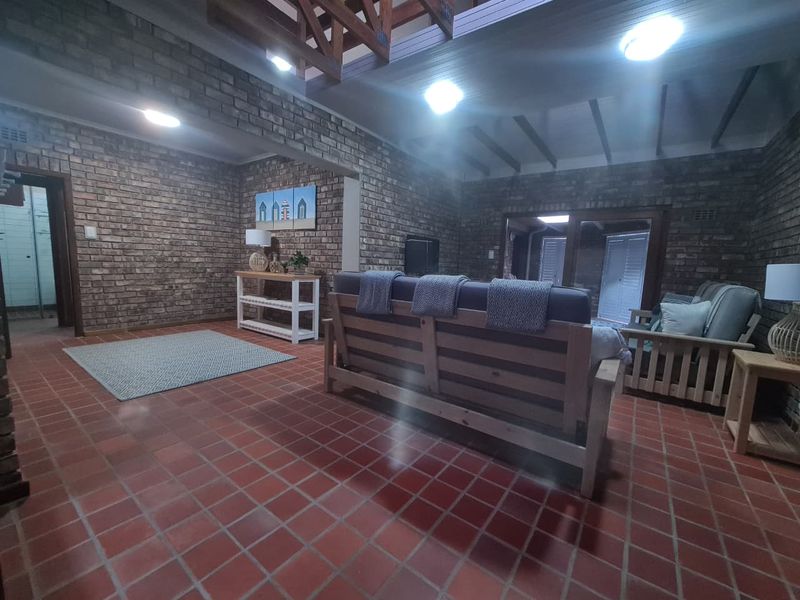 Spacious living area featuring rustic exposed brick walls, terracotta tile flooring, and high vaulted ceilings with exposed timber beams.