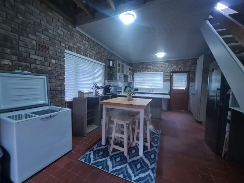 A rustic kitchen featuring exposed brick walls, tiled flooring, built-in cabinetry, and a central island, with an adjacent staircase leading to an upper level.