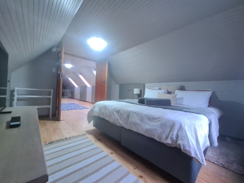 Attic-style bedroom featuring timber flooring, sloped timber ceilings, and built-in storage, with double doors leading to an adjacent living space.