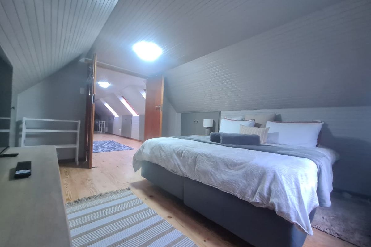 Attic-style bedroom featuring timber flooring, sloped timber ceilings, and built-in storage, with double doors leading to an adjacent living space.