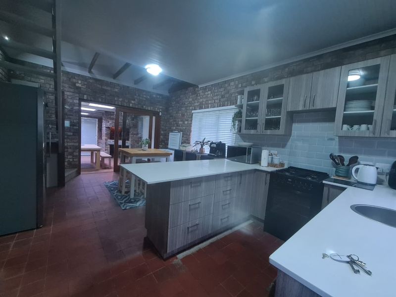 Open plan kitchen featuring exposed brick walls, modern cabinetry, a central island, and terracotta flooring, leading into an adjacent dining area.